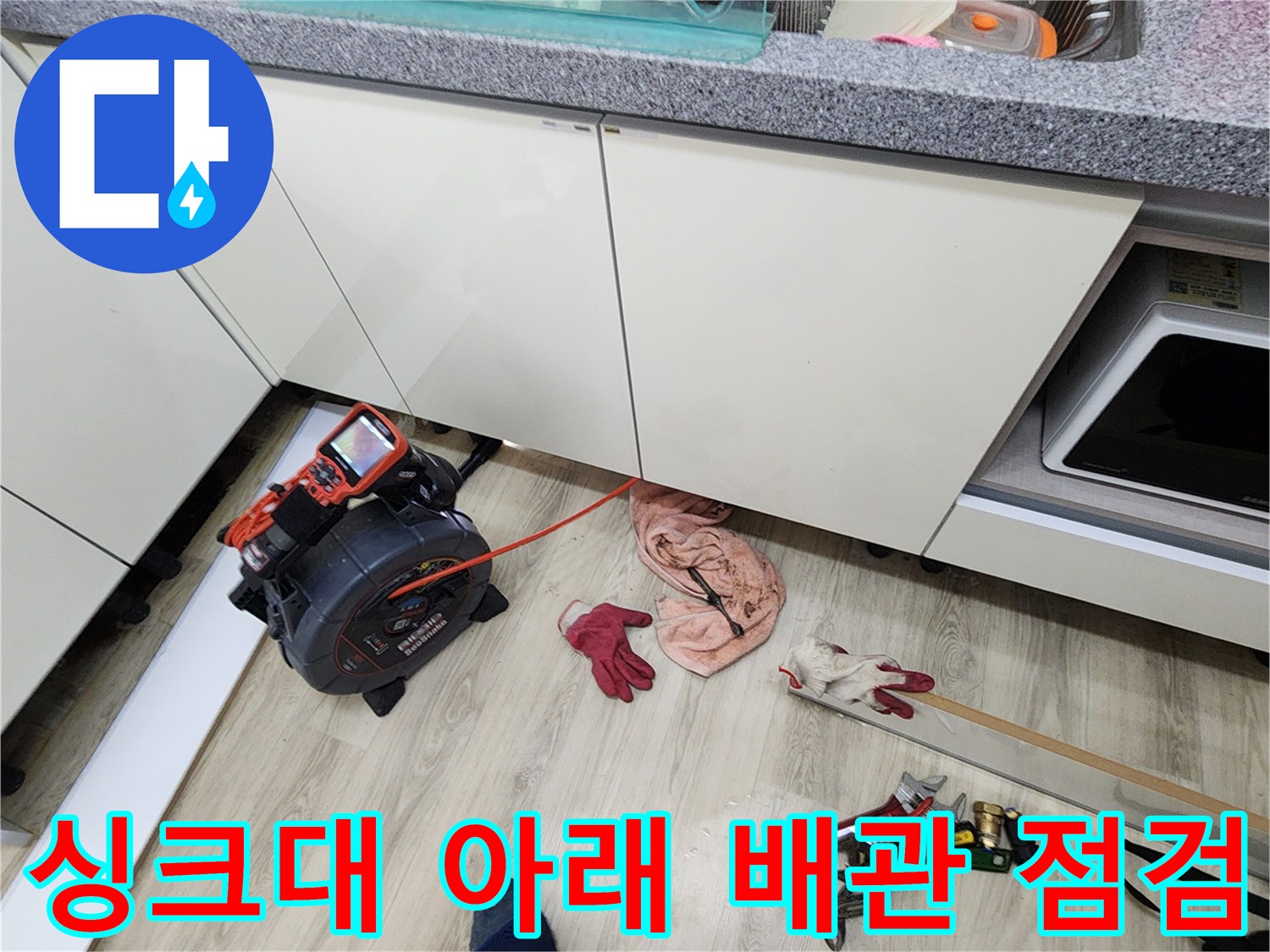 주방 싱크대 하부장 밑에서 진행 중인 배관 압력 테스트 장비와 작업 도구들