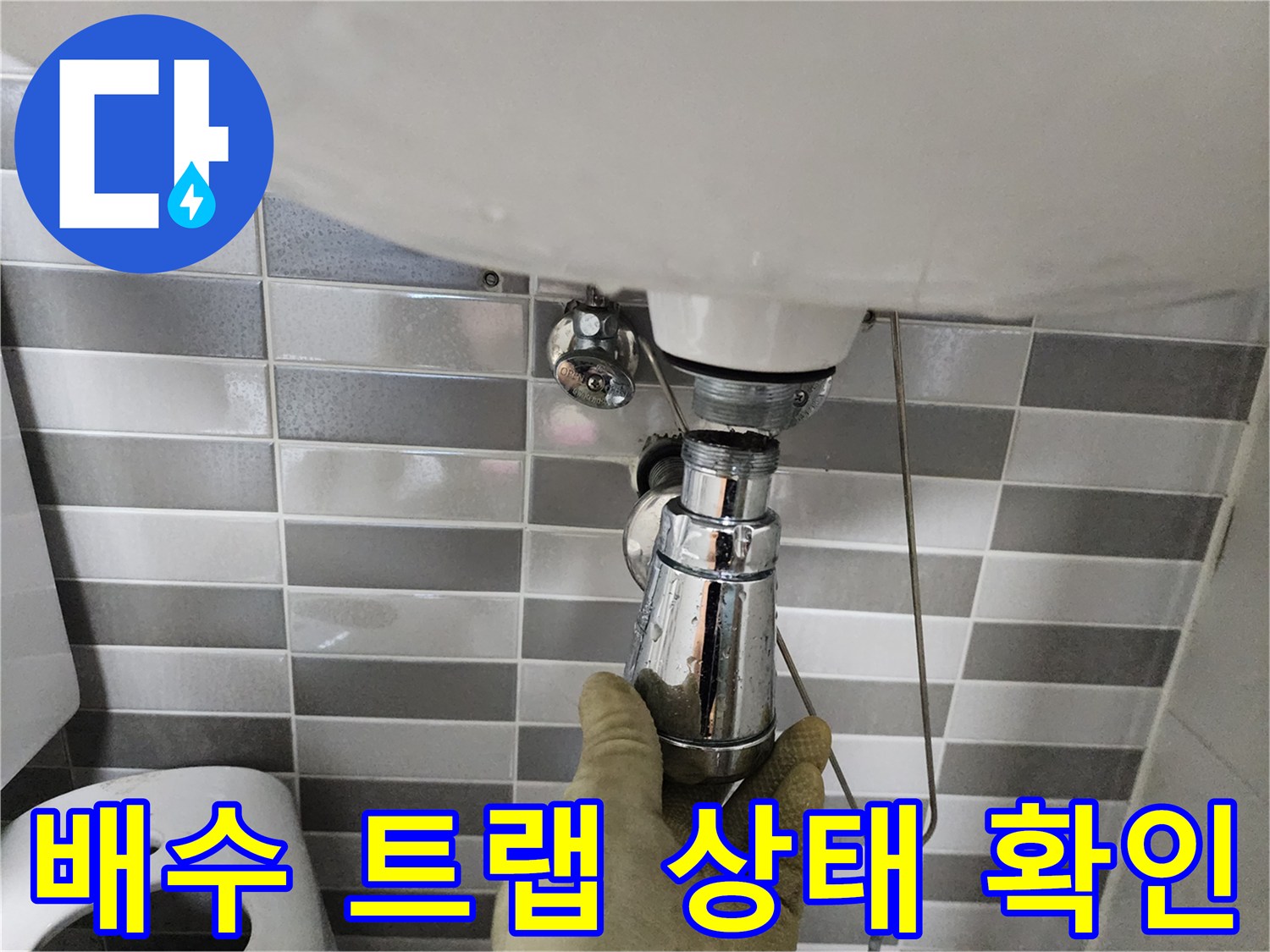 세면대 아래쪽 금속 배관을 엔지니어가 손으로 잡아 상태를 진찰하고 있습니다.