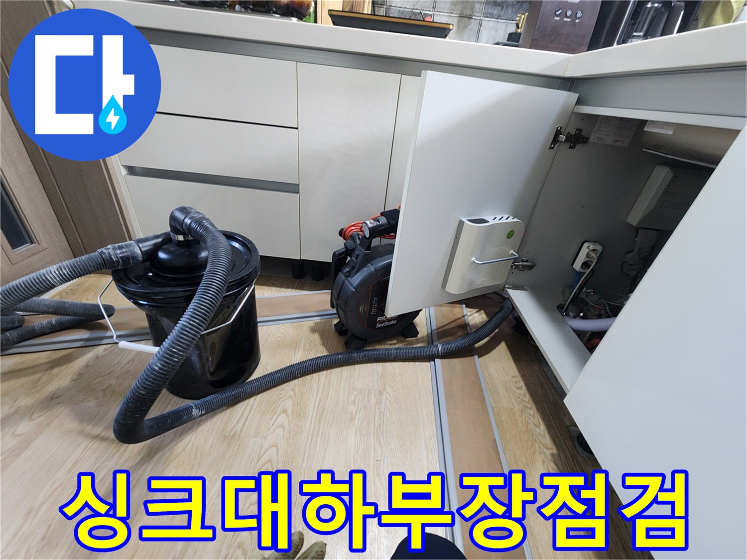 열려있는 싱크대 하부장과 내부 배관 및 작업 장비