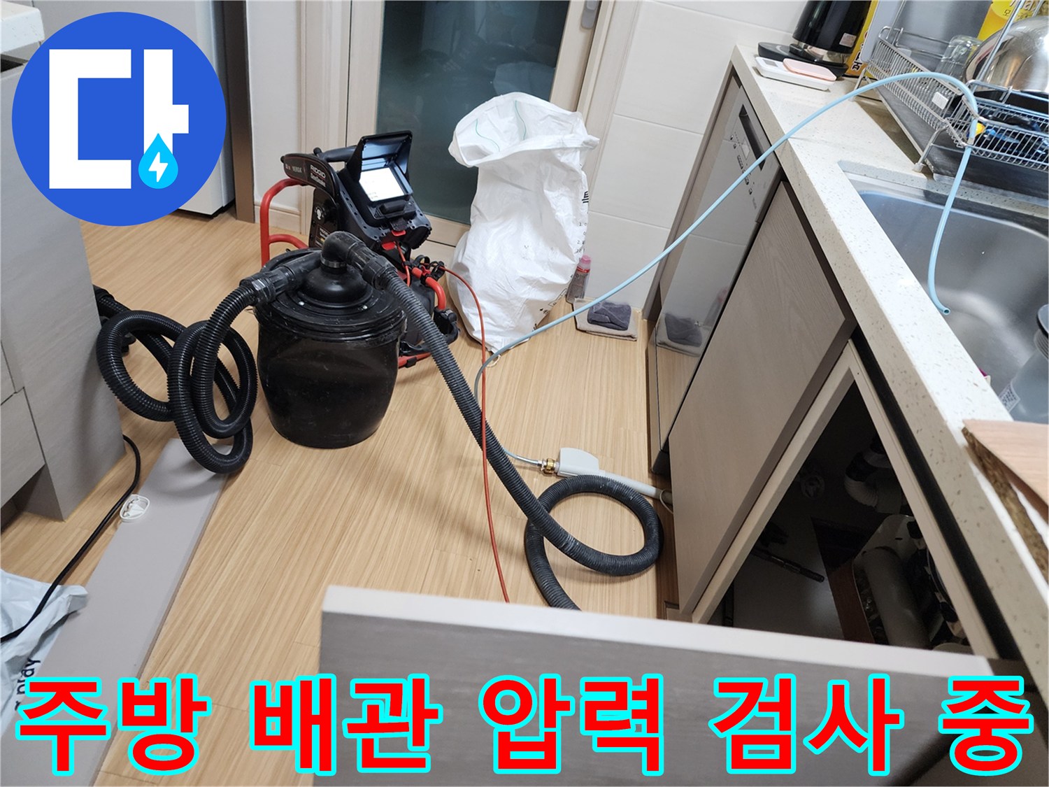 싱크대 하부의 배관 연결부에 테스트용 장비를 설치하여 점검하는 모습입니다.
