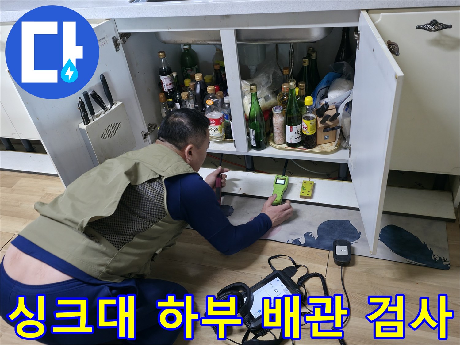 주방 싱크대 밑 공간에서 가스 탐지기와 압력계를 사용하여 누수를 확인하는 장면입니다.