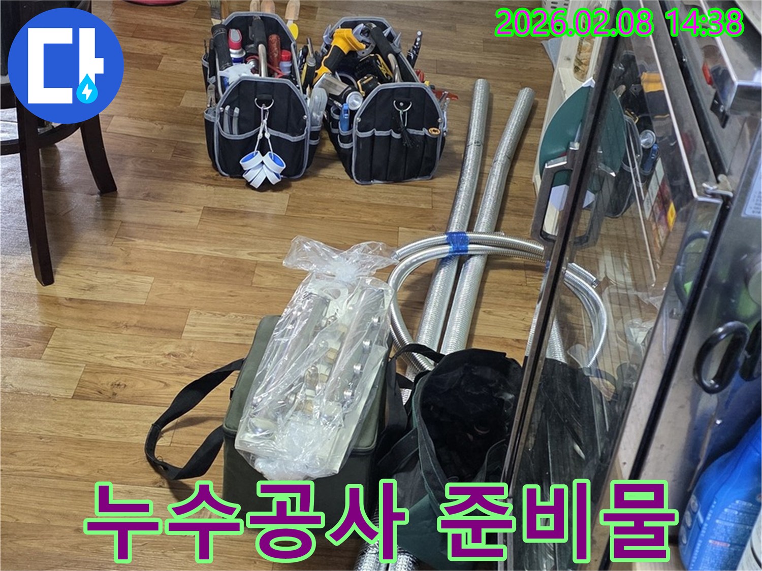 누수 공사를 위해 준비된 다양한 전문 장비와 새 배관 자재들이 깨끗한 마루 바닥에 놓여있는 모습입니다.