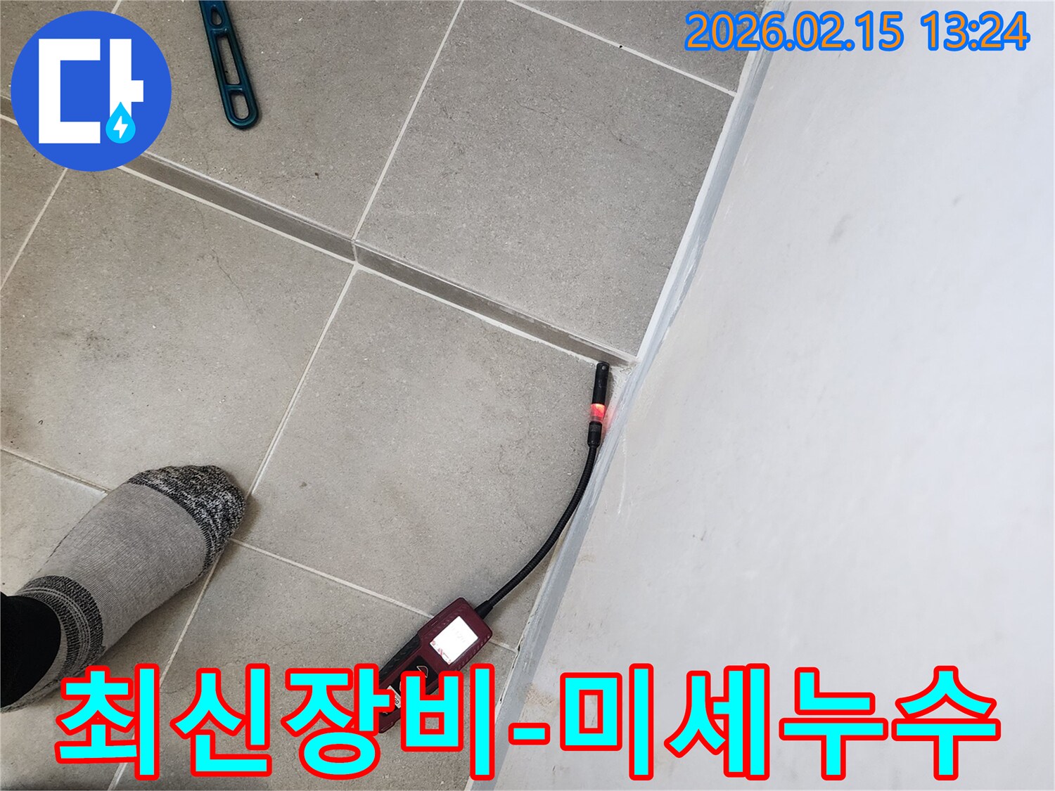 누수 엔지니어가 최신 누수탐지기를 이용해 바닥 타일과 벽면의 접합부에서 미세한 누수 지점을 발견하는 모습