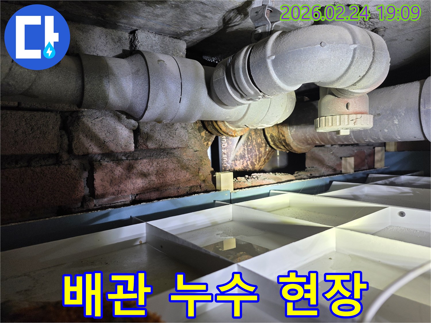 좁은-공간에-설치된-노후-배관에서-누수가-발생하여-물이-고인-상황을-보여주는-이미지