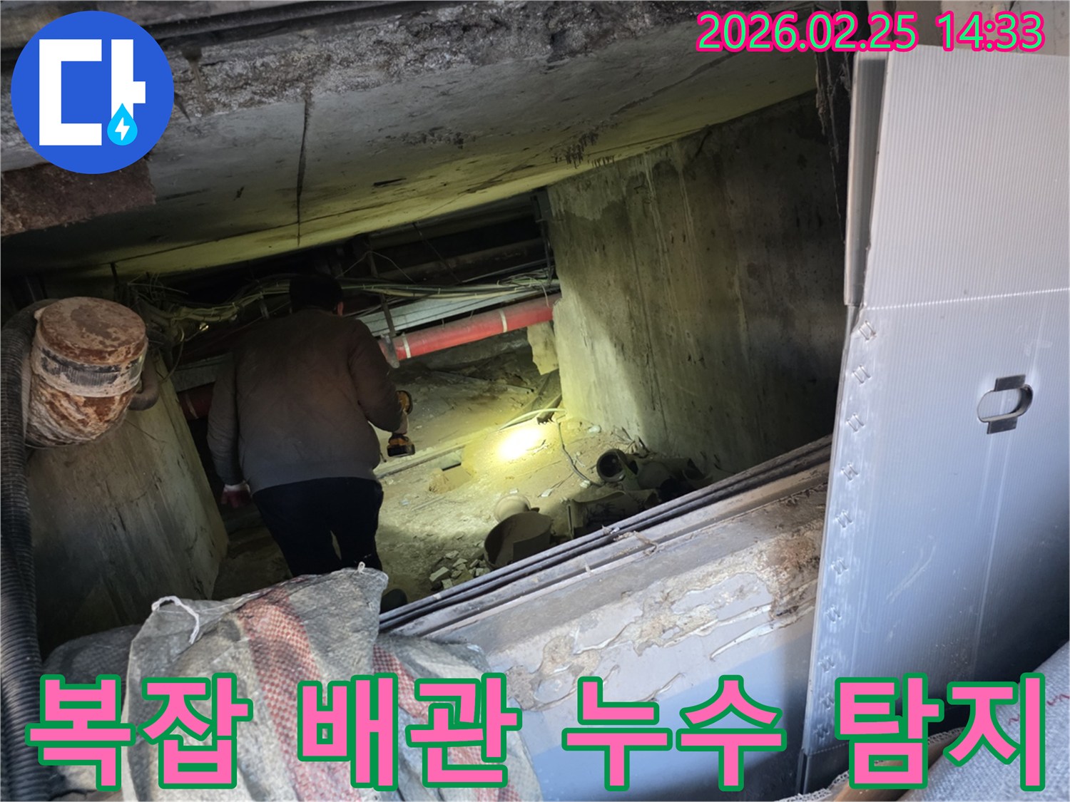 누수 전문 엔지니어가-어둡고 복잡하게 얽힌 배관 속에서-손전등을 비춰가며-숨겨진 누수 지점을-정확히 찾아내는 모습입니다.
