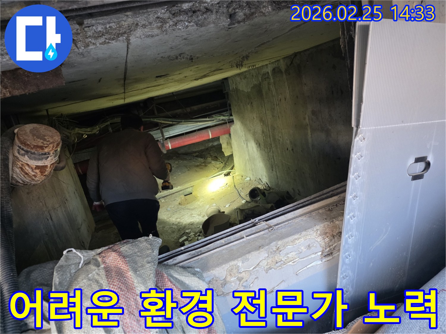 누수 전문 엔지니어가-어둡고 좁은 어려운 환경 속에서-손전등을 비춰가며-누수 지점을 찾아내기 위해-최선을 다하는 모습입니다.