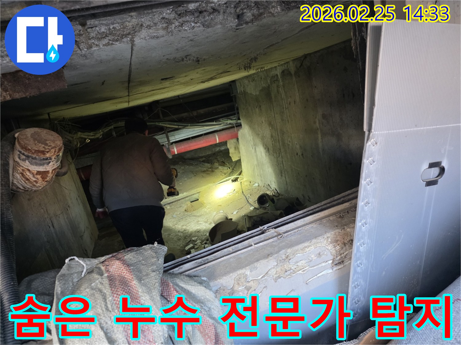 누수 전문 엔지니어가-어둡고 협소한 공간에서-손전등을 비춰가며-육안으로 확인하기 어려운-숨겨진 누수 지점을-정밀하게 찾아내는 모습입니다.