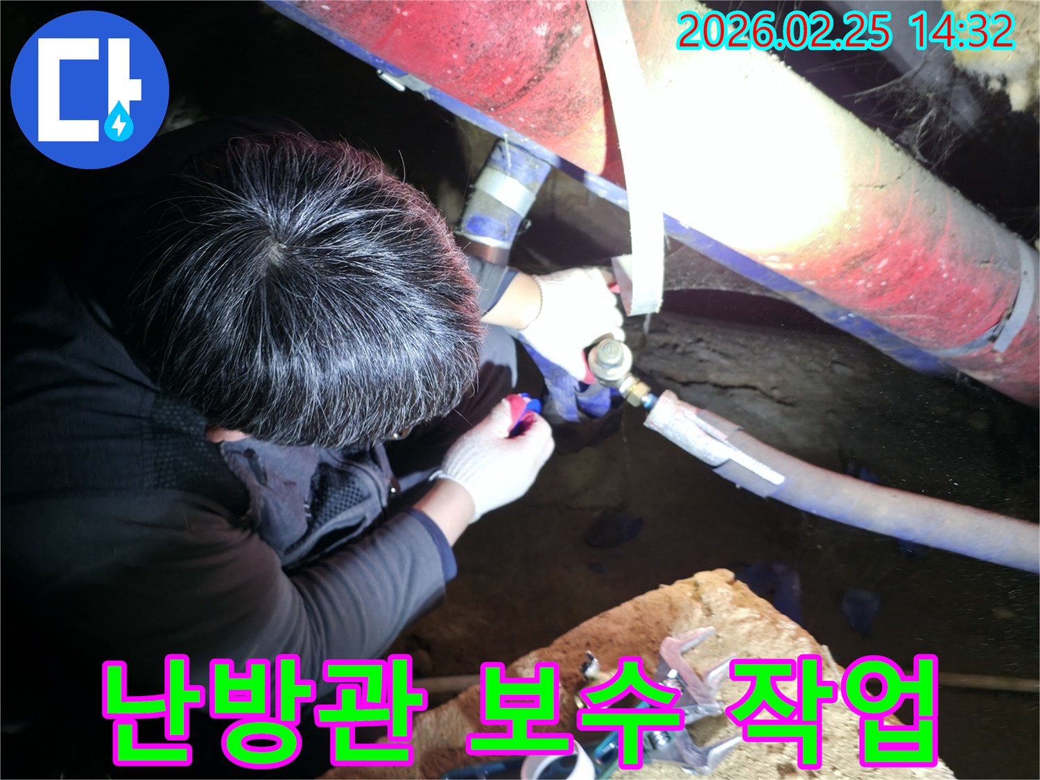 숙련된 누수 기술자가 좁은 공간에서 손전등을 비추며 난방관 연결 부위를 정밀하게 점검하고 수리하고 있습니다-난방누수해결-전문가수리