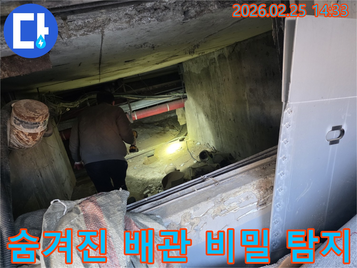 숙련된 누수 전문 엔지니어가-어둡고 협소한 공간에서-손전등을 비추며-숨겨진 배관의 미세한 누수 원인을-정밀하게 탐색하는 모습입니다.