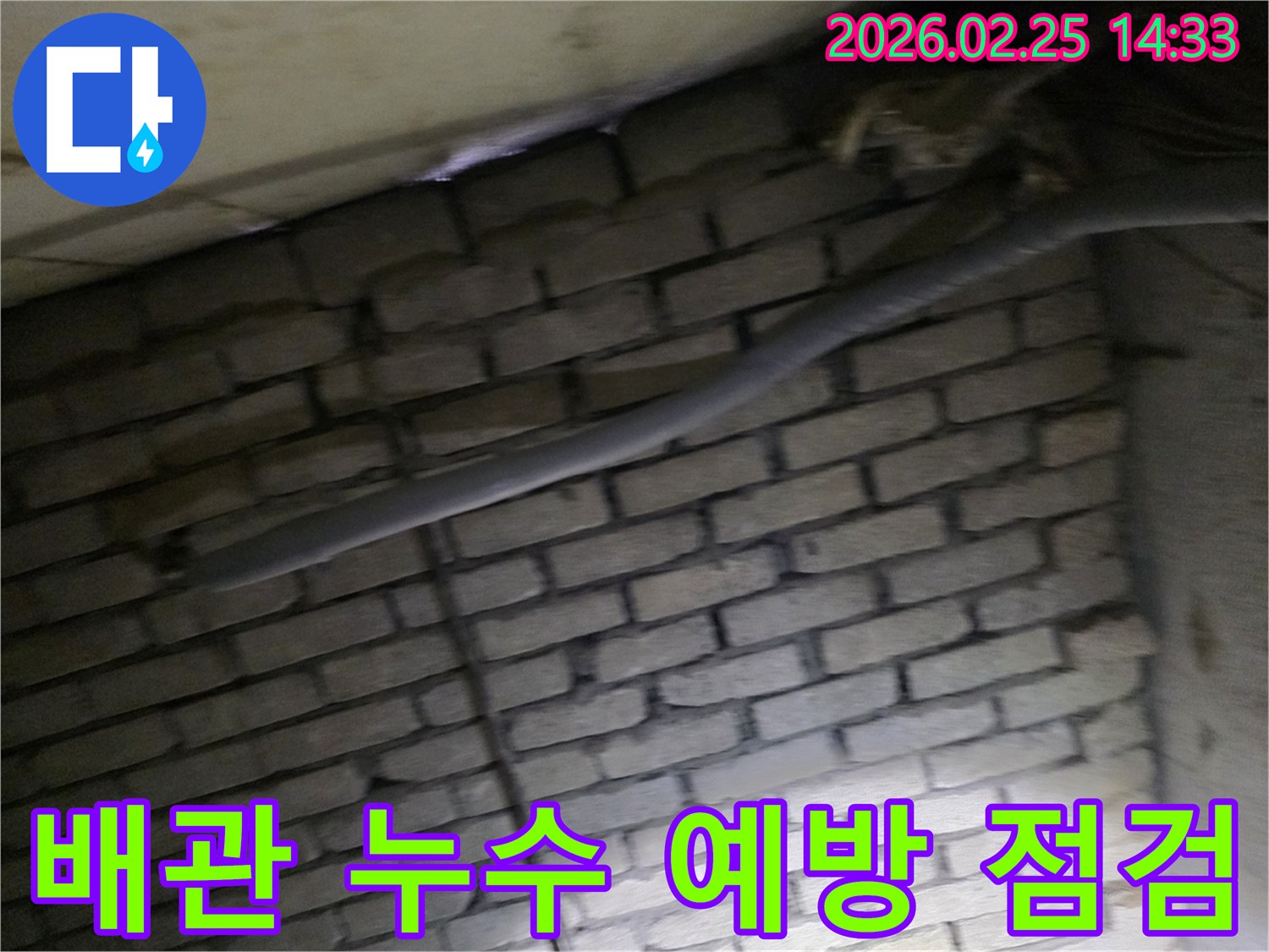 어두운 벽돌 벽면을 배경으로-단열된 배관의 상태를 점검하며-누수 예방을 위한-정밀 검사가 진행되는 현장 이미지입니다.