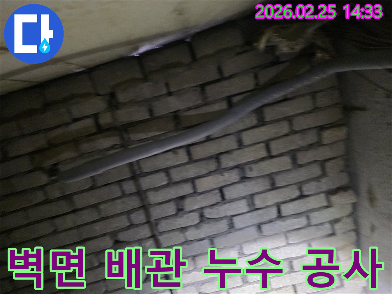 어두운 벽돌 벽면을 배경으로-단열재로 감싸인 배관과-다른 배선이 누수 여부를-확인하기 위해 촬영된 현장 이미지입니다.