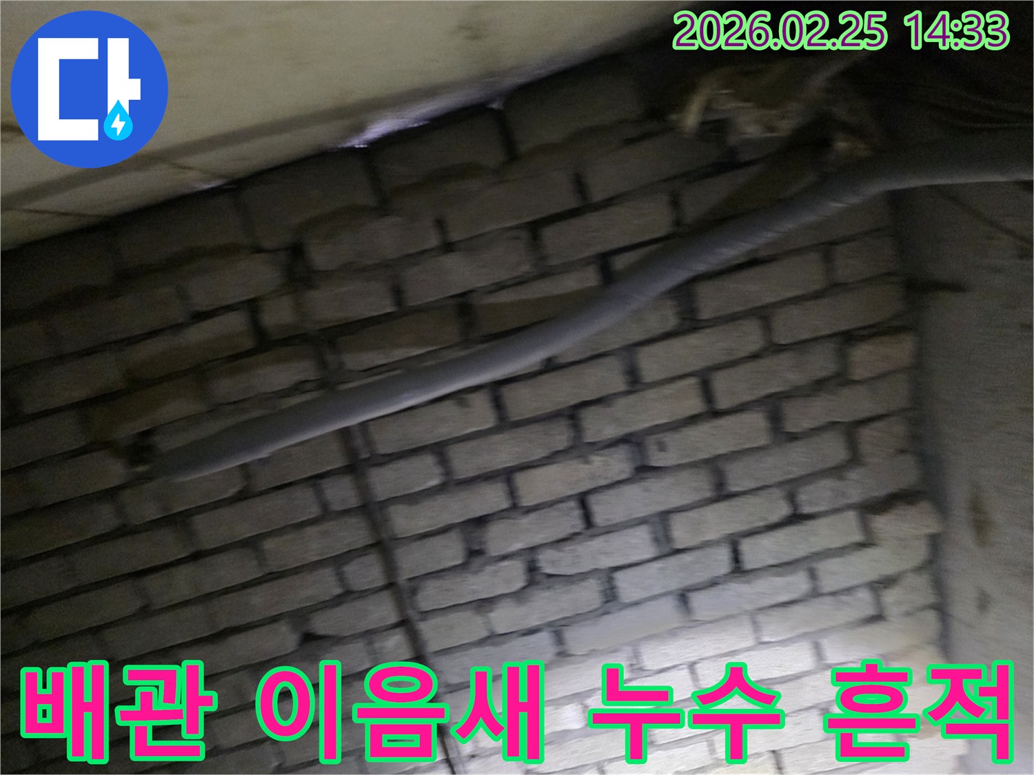 어두운 벽돌 벽면을 배경으로-단열재로 감싸인 배관의-이음새 부위에서 발생한-누수 흔적을 확인하는 현장 이미지입니다.