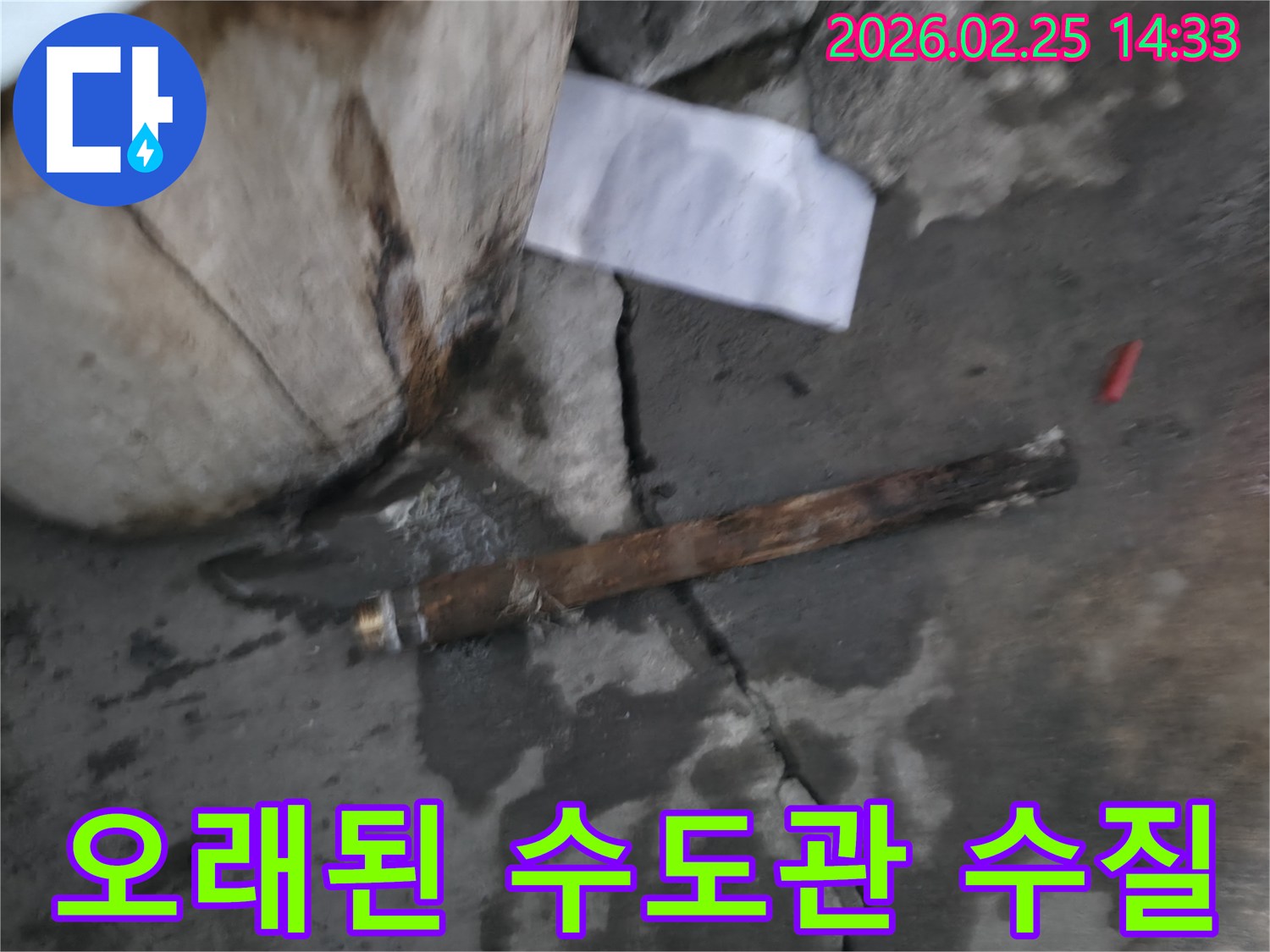 오래되어 녹슬고-파열된 수도관이-젖은 콘크리트 바닥에 놓여있는-누수 현장 사진입니다.
