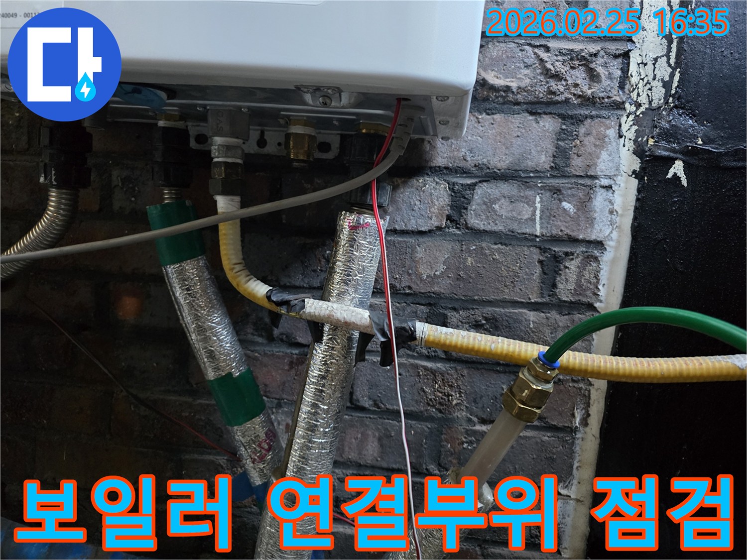 이 이미지는-벽에 부착된-보일러 하부의-복잡한 배관 연결부와-전선-그리고-은색 단열재로-감싸진-파이프들을-선명하게-보여줍니다.