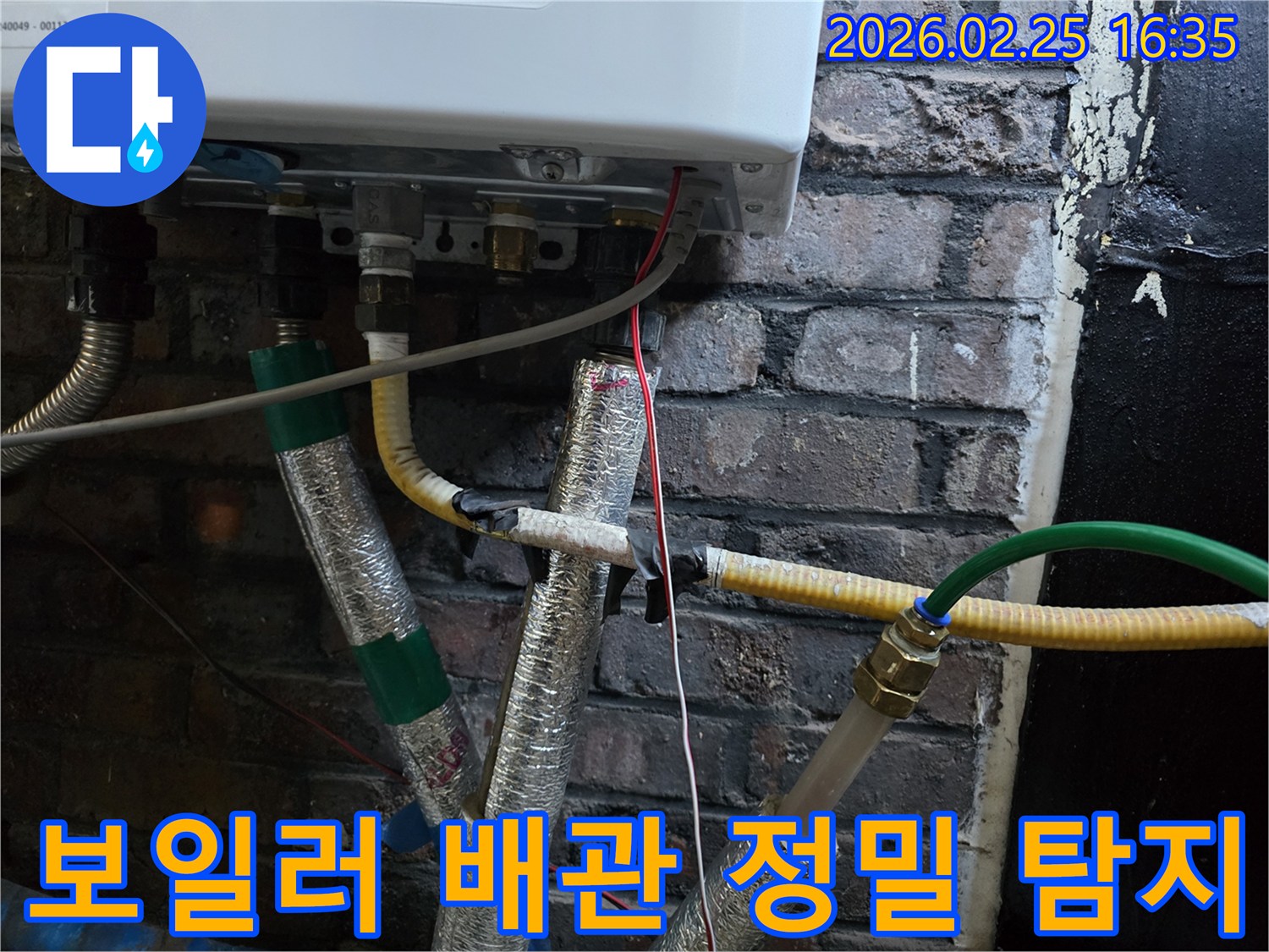 이 이미지는-벽에 설치된-보일러 하단부의-복잡한 배관 연결부와-전선-그리고-은색 단열재로-감싸진-파이프들을-보여주며-누수 지점을-찾기 위한-정밀한 탐지 작업이-진행되고-있음을-암시합니다.