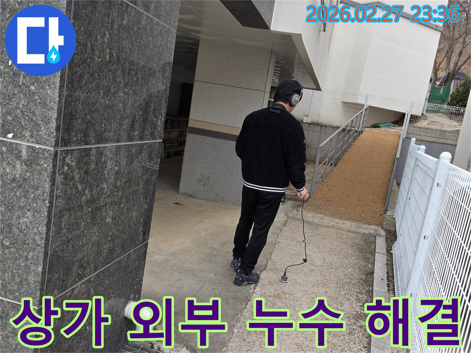 누수 엔지니어가-청음식 탐지기로-상가 건물 외부의-누수 지점을 신속히 찾아내어-영업 지장 없이 문제를 해결하는 모습