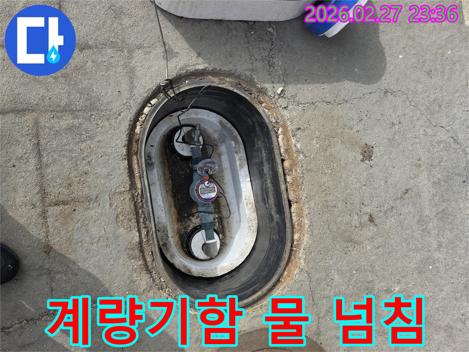 지하에 매설된 수도 계량기함 내부에-물이 가득 차 넘치기 직전의 상태를 보여주는 사진입니다.