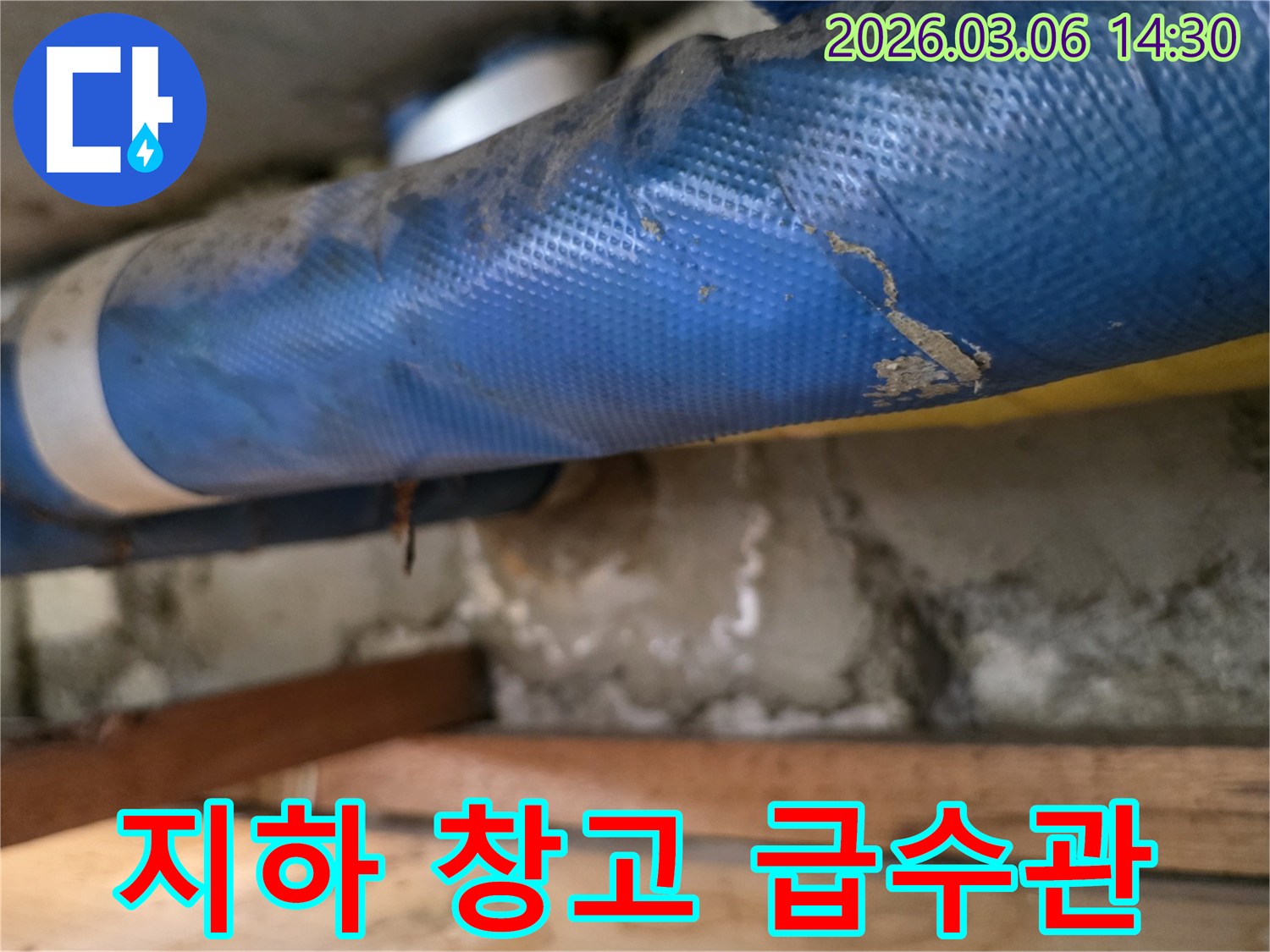 상가 지하 창고의-파란색 급수관과-젖은 콘크리트 벽면-그리고 나무 지지대를-꼼꼼히 점검하는 모습