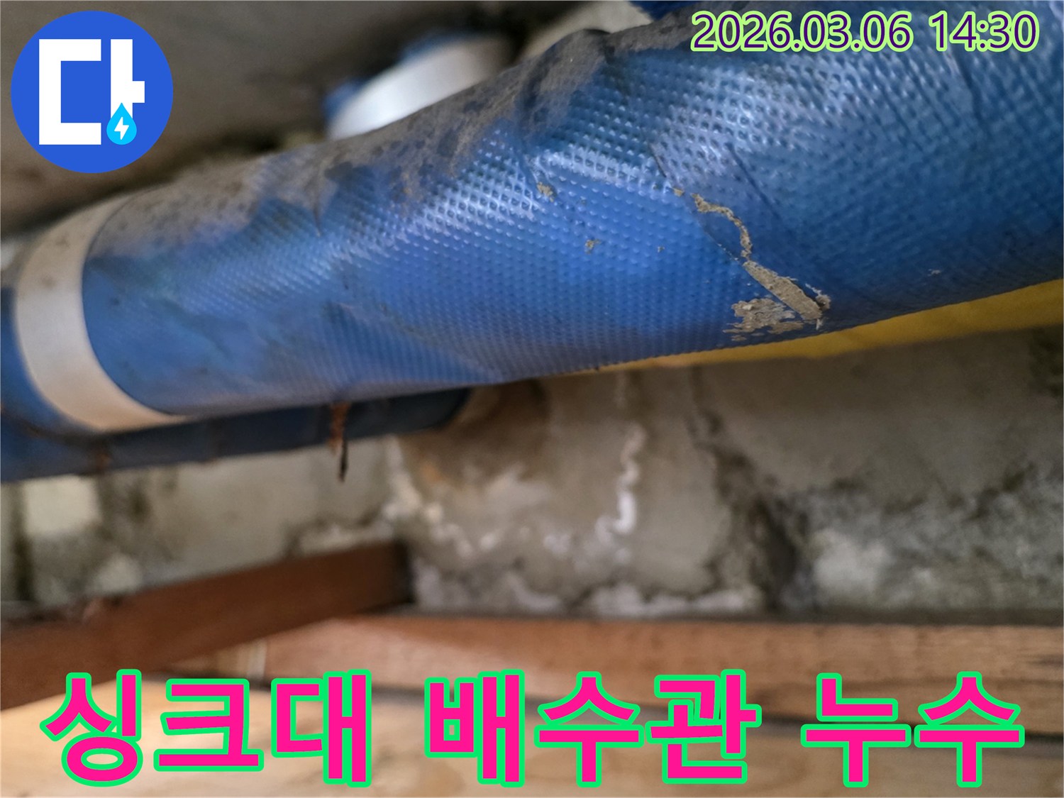 아파트 주방 하부-파란색 배관과-젖은 콘크리트 벽면-그리고 나무 지지대를-꼼꼼히 점검하는 모습