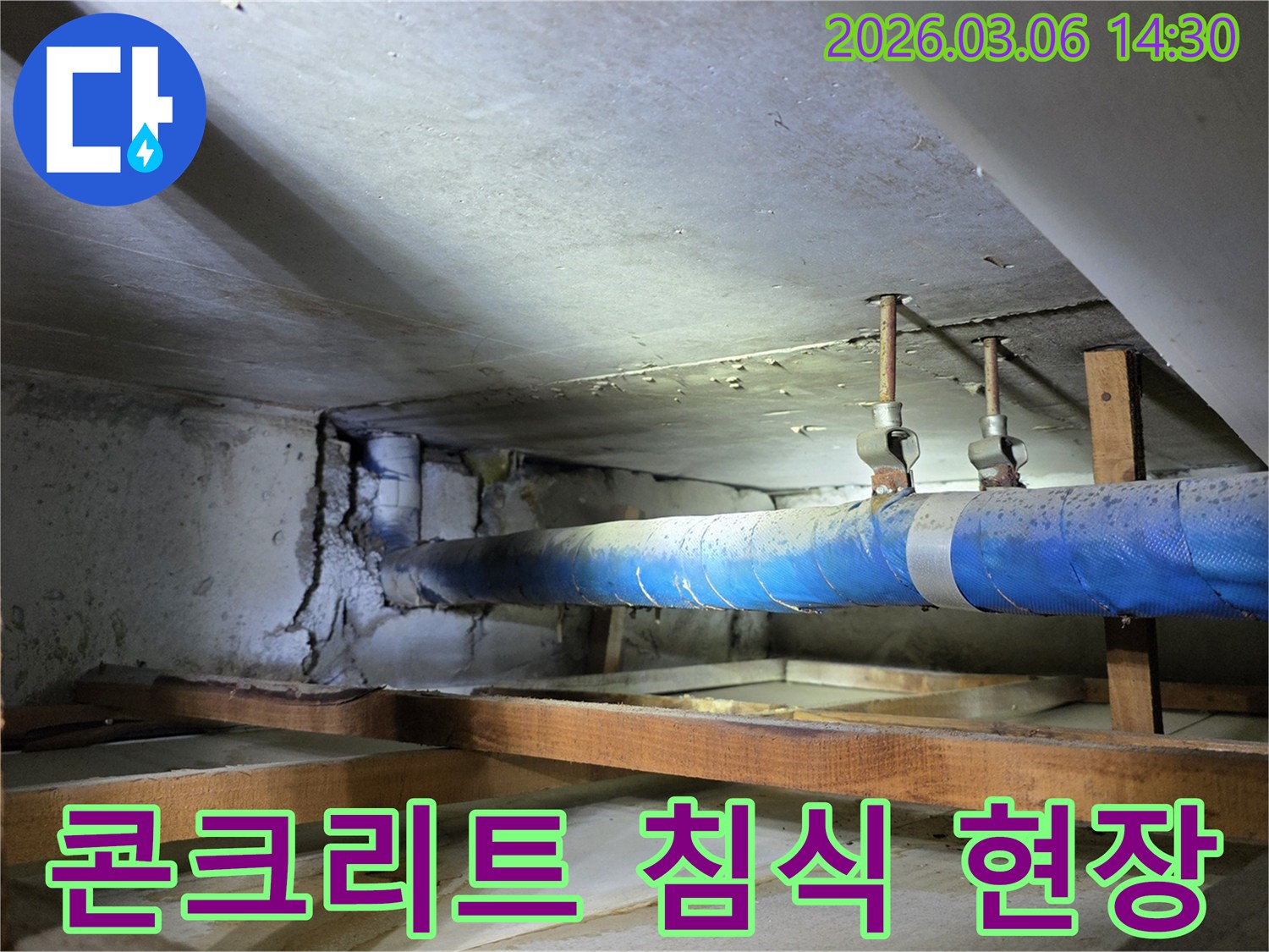 지하 공간의 파란색 배관에서-새어 나온 물로 인해-심하게 침식된 콘크리트 벽면을-누수 엔지니어가-정밀하게 점검하는 모습