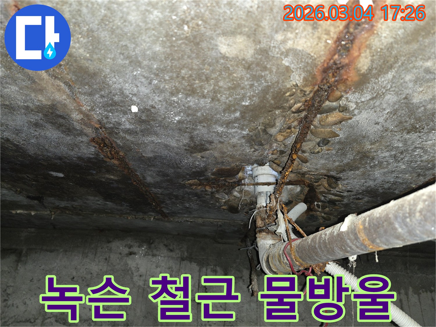 이 이미지는- 빌라 천장에서 발생한- 누수로 인해- 녹슨 철근과- 배관 주변에 맺힌- 물방울을- 선명하게 보여줍니다