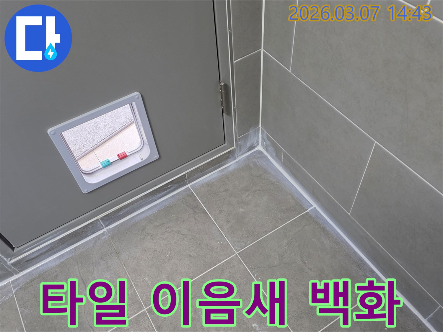 회색 타일의 이음새와 벽면 하단-그리고 문 주변에 나타난-흰색 백화 현상은-물이 스며들고 있음을 나타내는 누수 증상입니다.