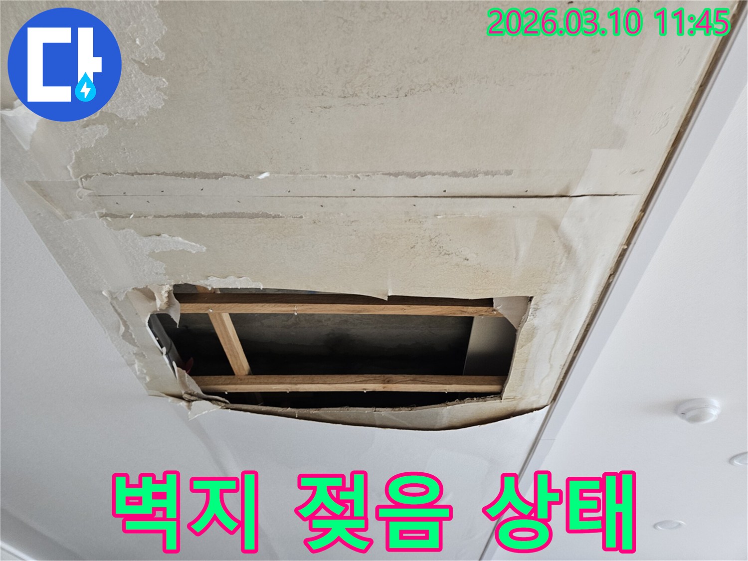오래된 누수로 인해-벽지가 젖고 훼손되어-천장 내부의-목재 구조물이-드러난 현장 사진입니다.