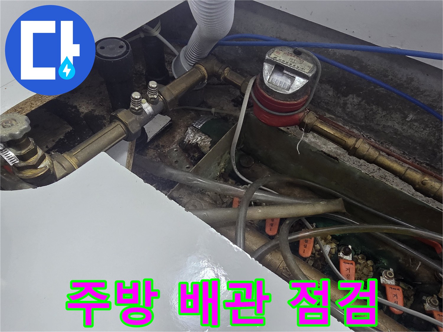 싱크대 하부장 내부의 수도 계량기와 복잡한 배관 연결 상태를 보여주는 사진입니다.