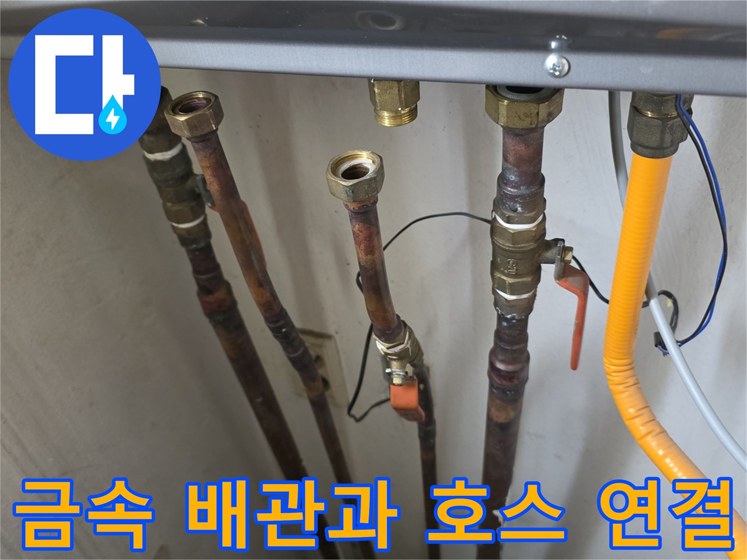 보일러 하단의 구리색 배관들과 노란색 급수 호스가 복잡하게 연결된 사진입니다.