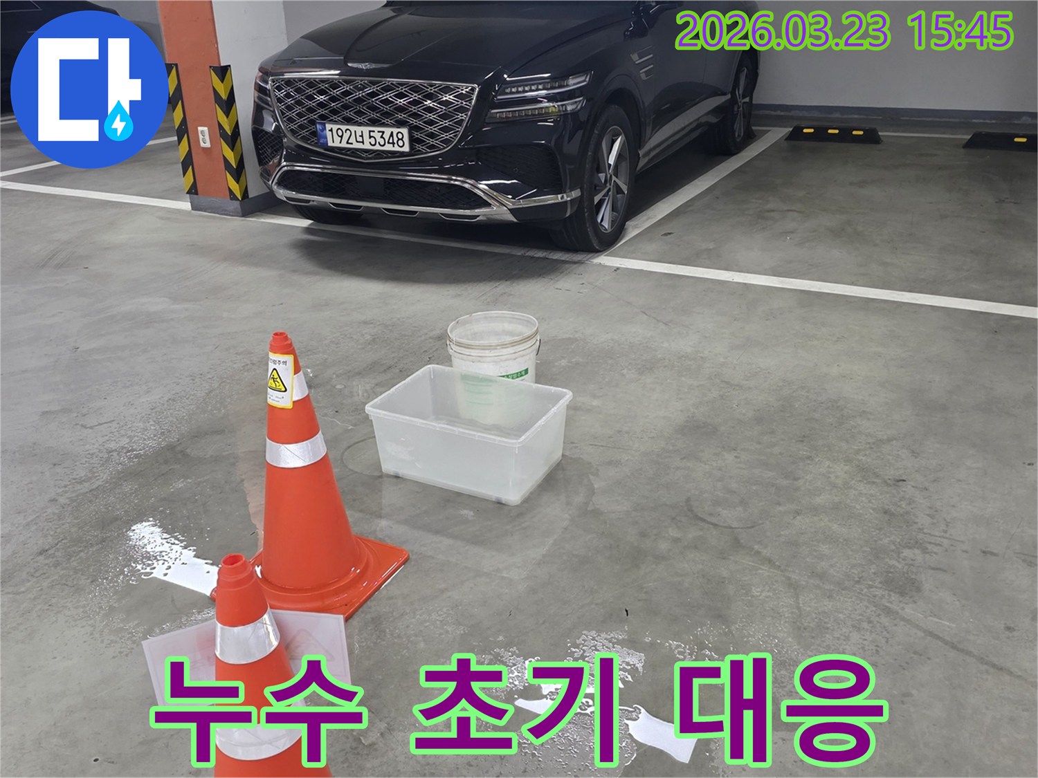 지하주차장 바닥에 물이 고여-안전 콘과 물받이가 설치된-누수 현장을 보여주는 이미지입니다.