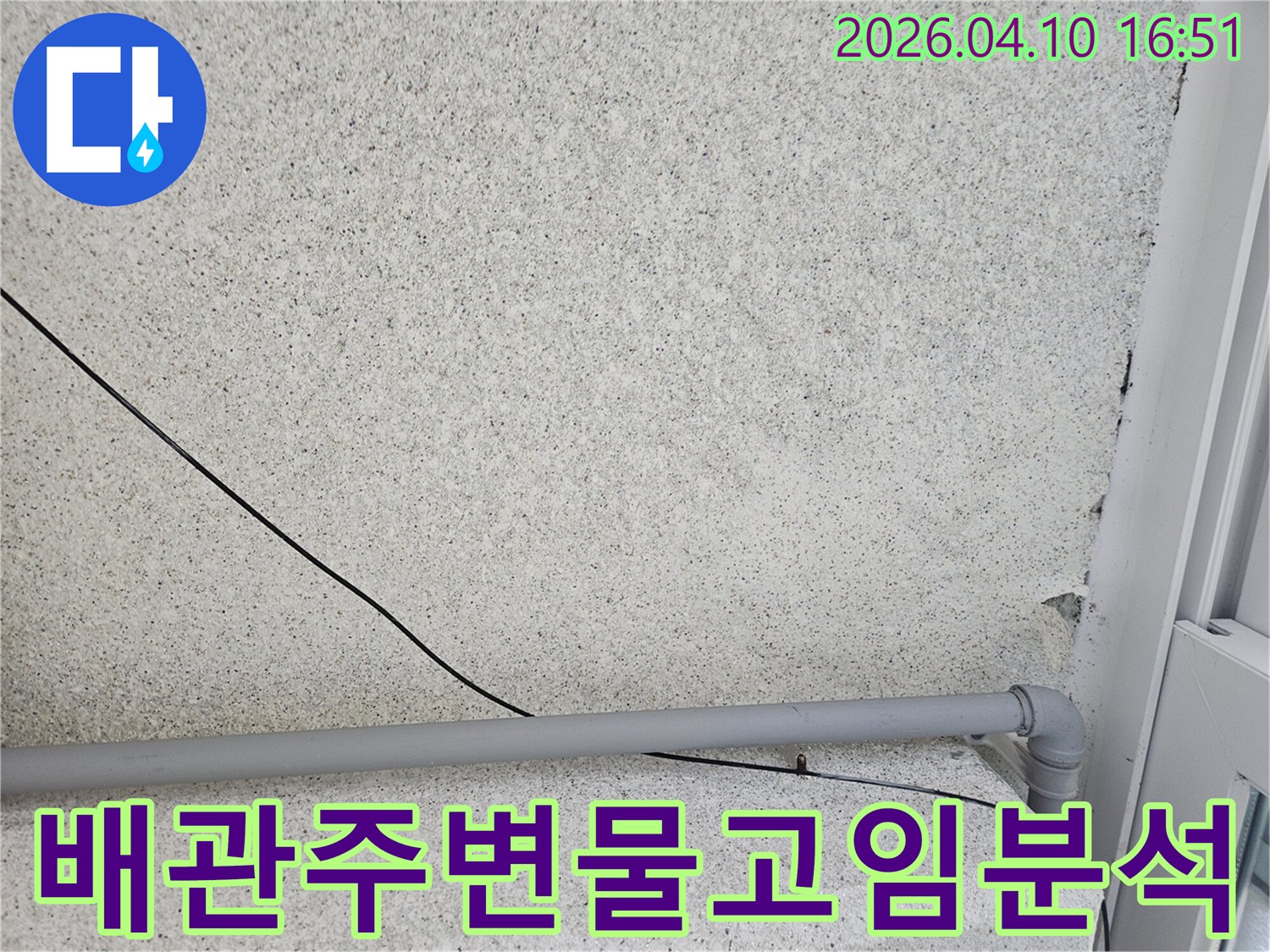 회색 벽에-설치된 회색 배관과-검은 전선이-누수 원인을 찾기 위해-배관 주변의-물고임 현상을-분석하는 모습입니다