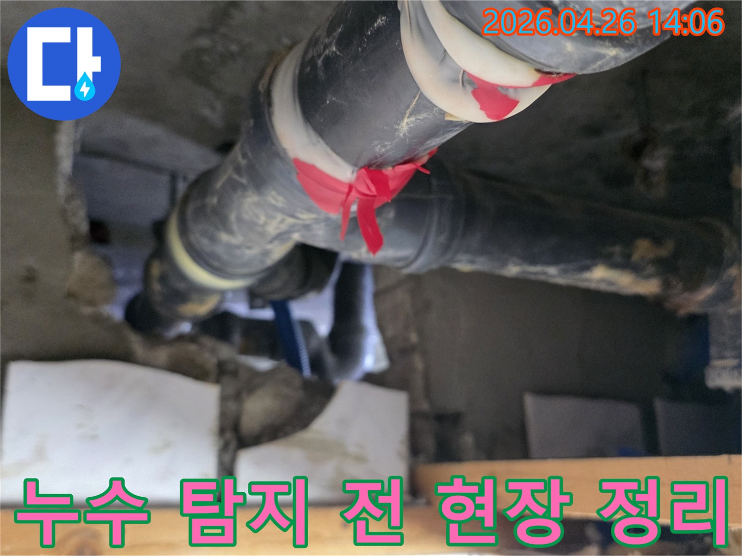 이 이미지는 아파트 배수관에서-누수 탐지를 시작하기 전-빨간 테이프로 의심 지점을 표시하고-주변을 정리하는-전문가의 모습을 담고 있습니다.