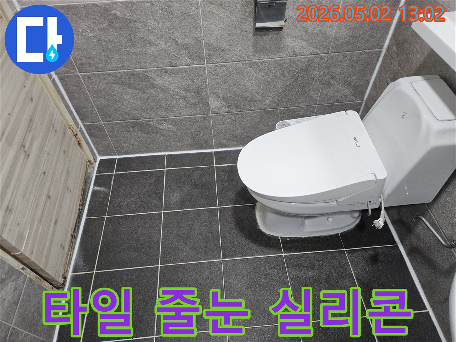 이 이미지는 욕실 바닥과 벽 타일의 줄눈-그리고 변기 주변에 새로 시공된 깨끗한 실리콘 코킹 마감 상태를 보여줍니다.