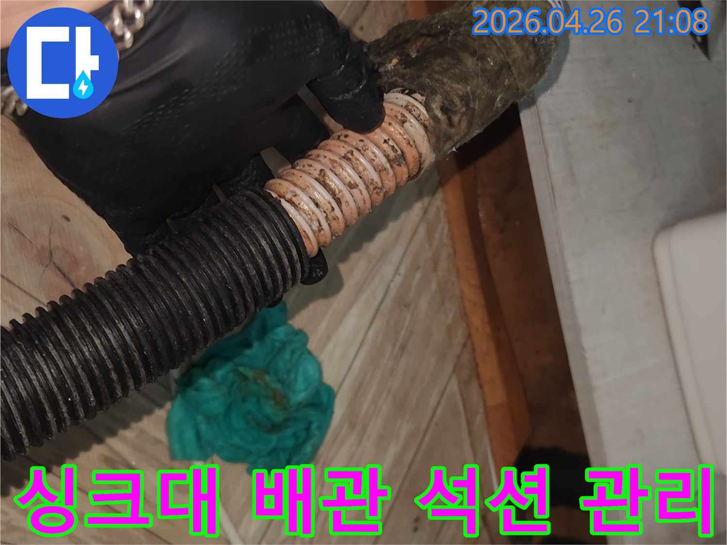 검은 장갑을 착용한 엔지니어가-오염된 싱크대 배수 호스를-석션 장비로 깨끗하게 청소하여-누수를 예방하고 관리하는 모습