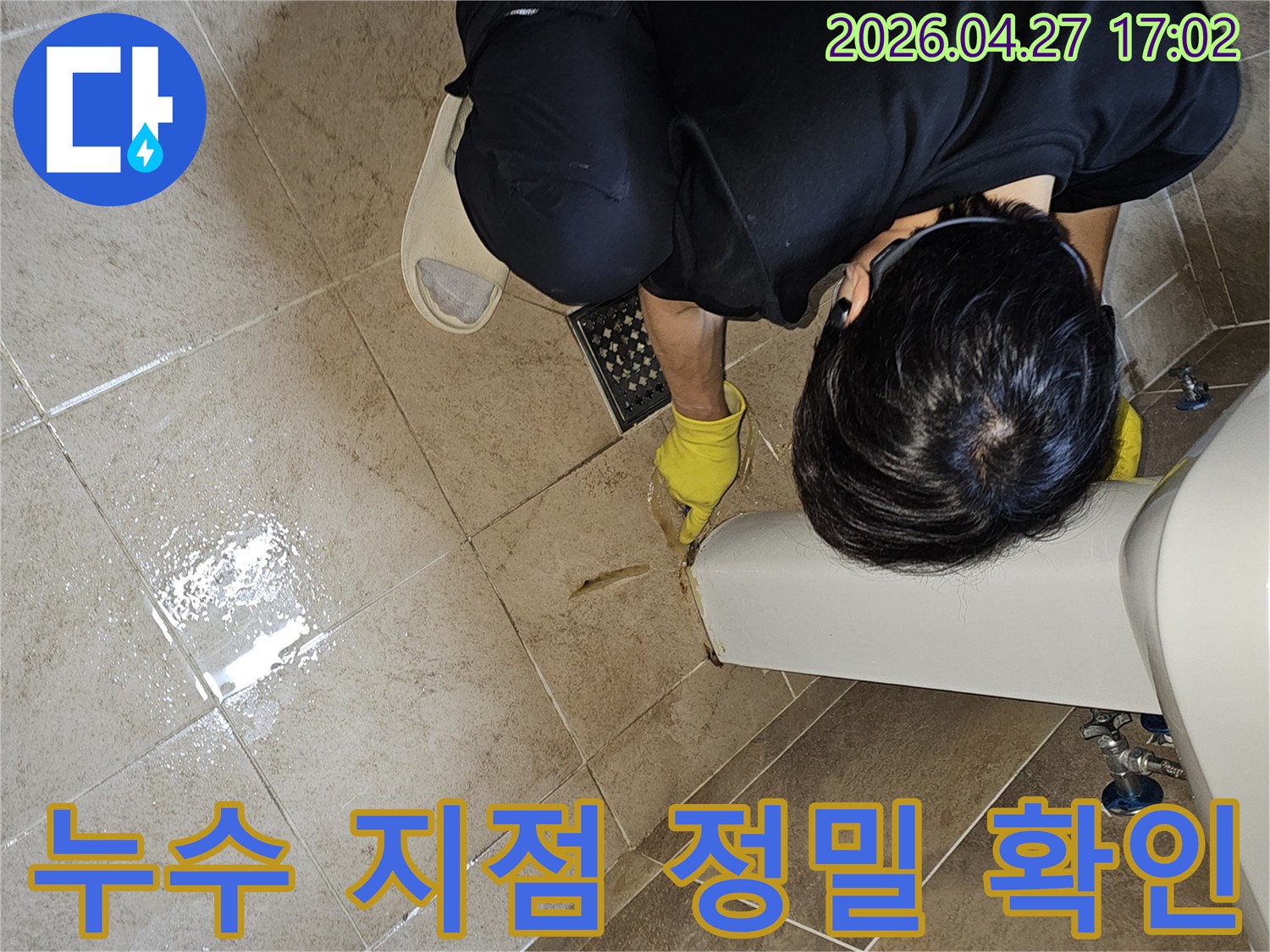 누수 전문가가-젖어있는 욕실 바닥 타일과-세면대 하단부를-집중적으로 살펴보며-누수 지점을 특정하고 있습니다