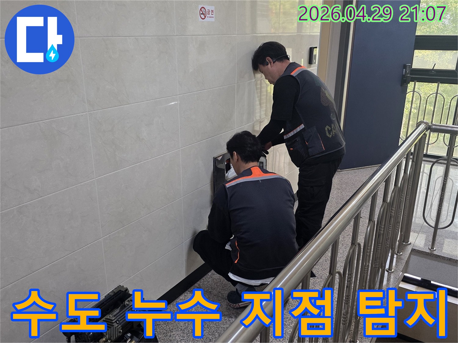 두 명의 전문 기술자가 건물 벽면 내부의 수도 누수 의심 지점을 정밀하게 탐지하고 있습니다-물 낭비 방지와 수도 요금 절감을 위한 필수 작업입니다.
