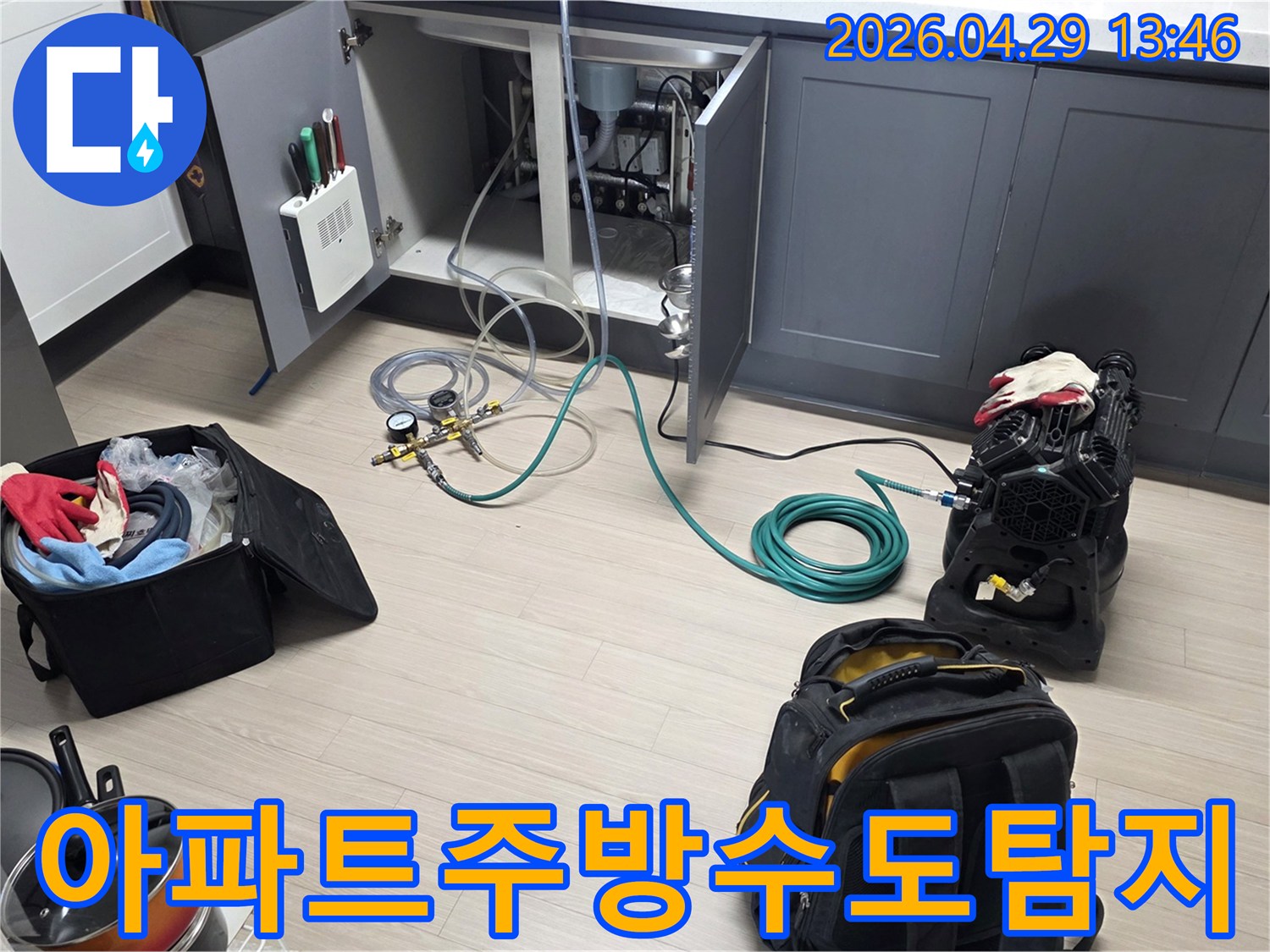 동안구 아파트의 주방 싱크대 하부에서-수도 배관의 누수를 확인하기 위해-압력 게이지와 호스-그리고 공기 압축 장비를-설치하는 작업이 진행 중입니다