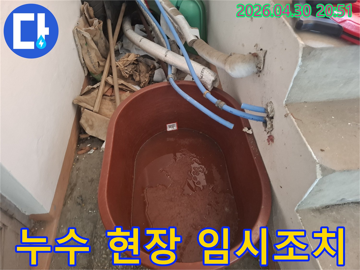 누수 현장에서-물이 떨어지는 것을-받아내기 위해-설치된-갈색 물통과-주변의-배관들이 보입니다