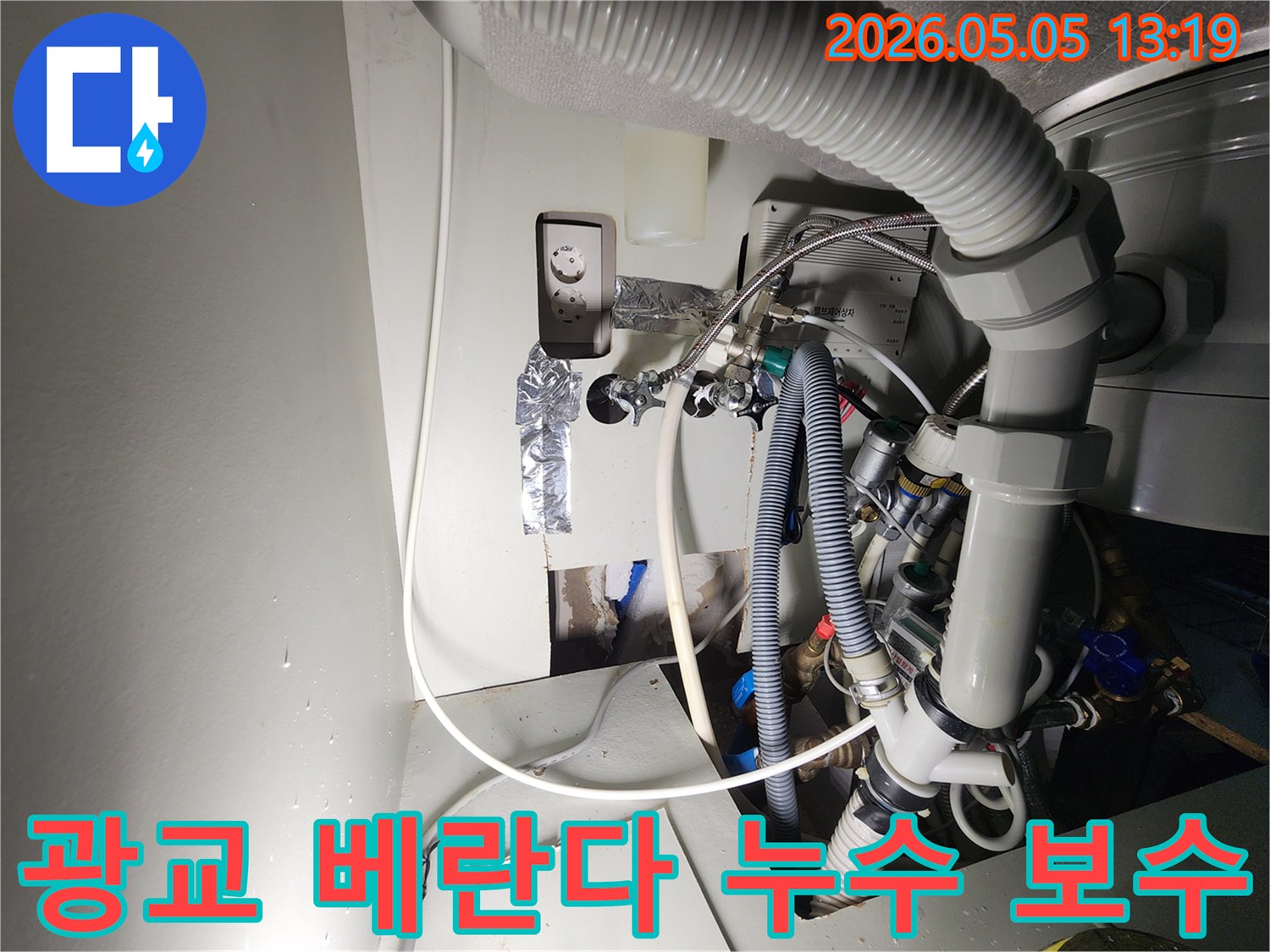 이 이미지는-광교-아파트-베란다-근처에서-발생한-누수-현장을-보여주며-벽면을-개방하여-드러난-복잡한-배관과-전기-시설-사이에서-물이-새는-모습을-촬영한-것입니다
