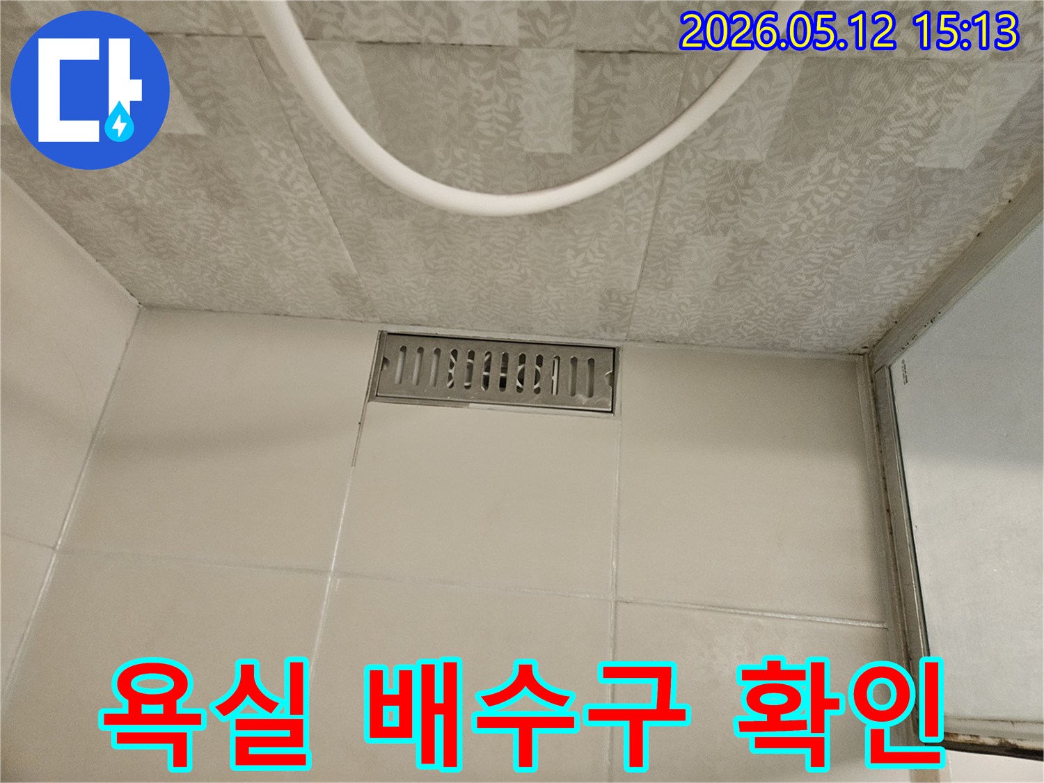 욕실 바닥의 스테인리스 선형 배수구와-주변의 흰색 타일-그리고 천장 마감재가 보이는-누수 점검 현장의 모습입니다.