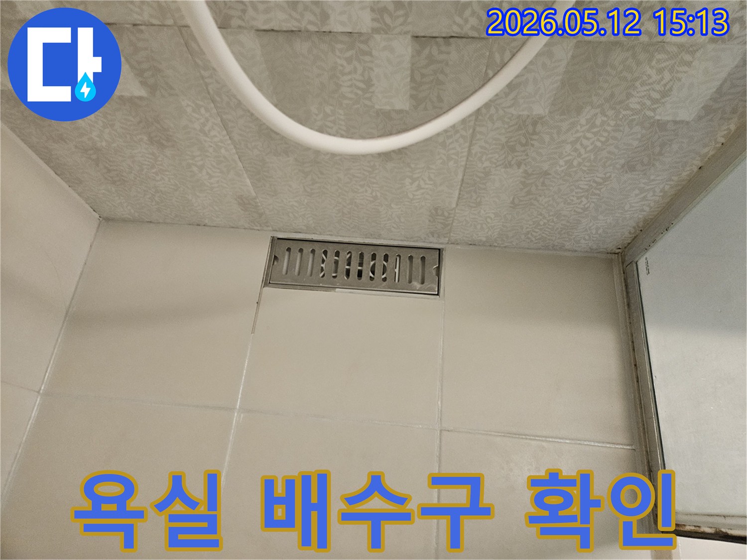 욕실 바닥의 스테인리스 선형 배수구와-주변의 흰색 타일-그리고 천장 마감재가 보이는-누수 점검 현장의 모습입니다.