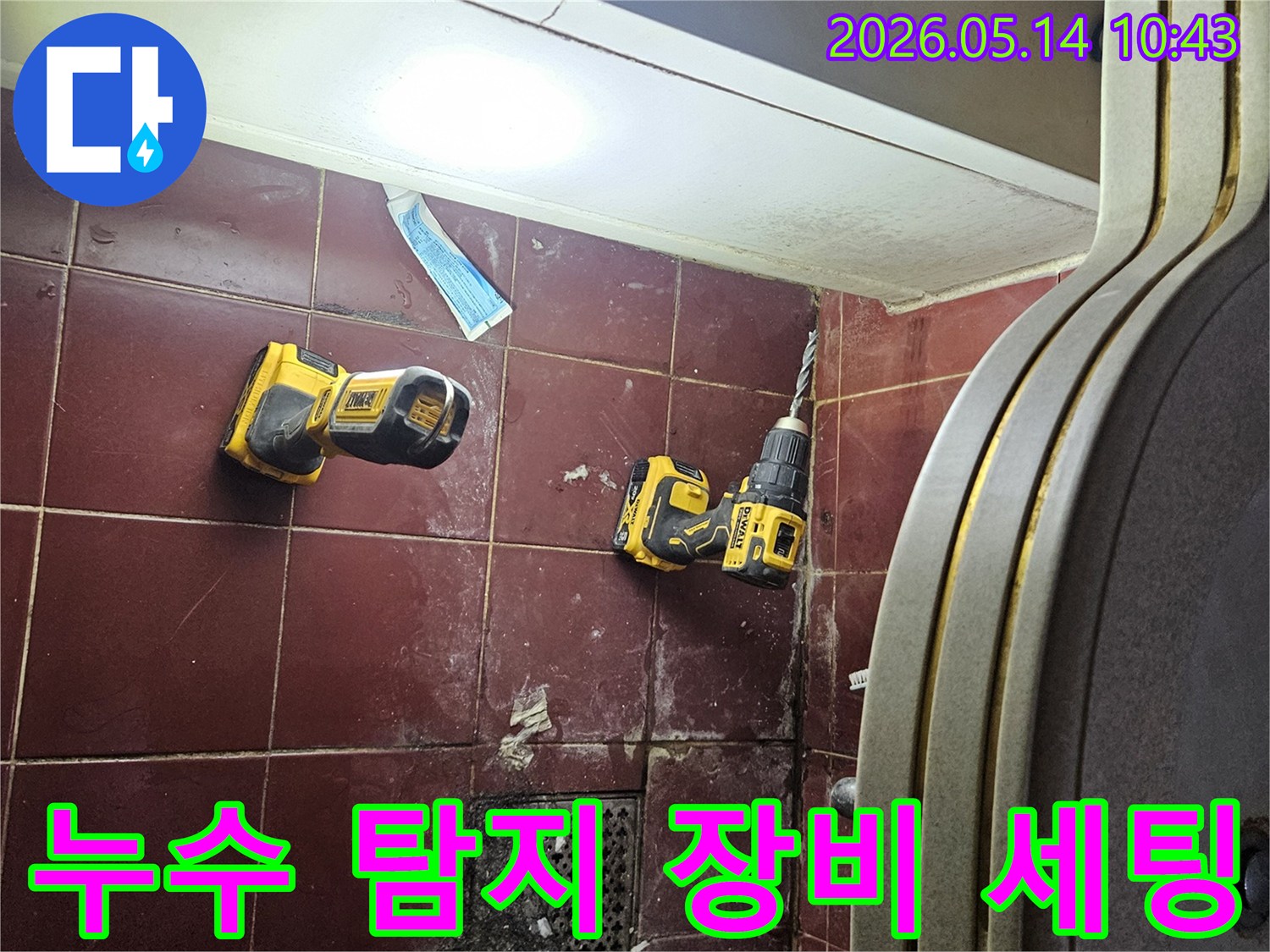 붉은 타일 바닥 위에 놓인 전동 드릴과 밝은 작업등-누수 탐지를 위한 장비 세팅이 완료된 모습입니다