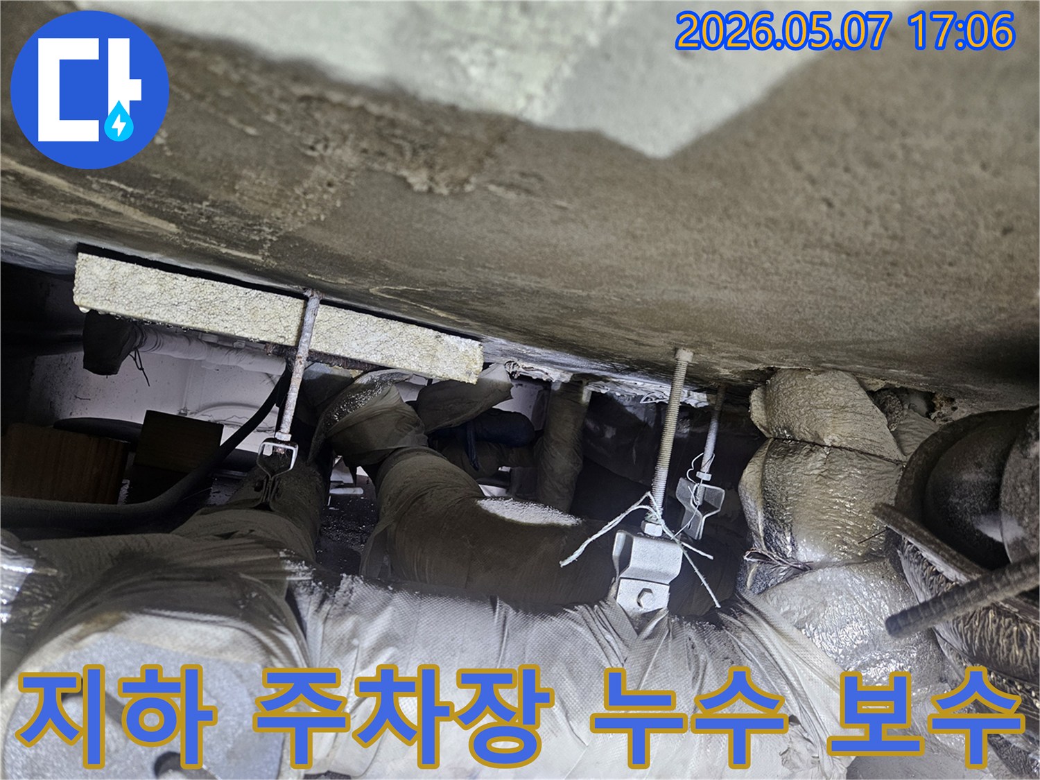 지하 주차장 천장의 복잡한 배관 구조물에서 누수 지점을 찾아 보수 작업을 준비하는 모습