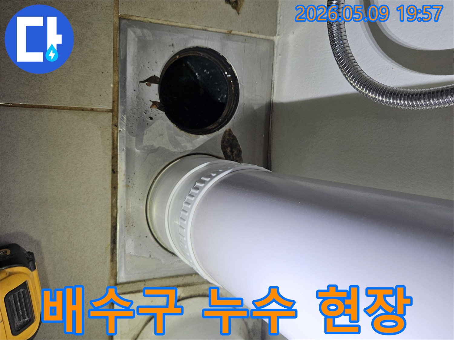 이 이미지는 욕실 바닥의 배수구와 인접한 배관에서 발생한 물 고임 현장을 보여주며-누수 가능성을 시사합니다.