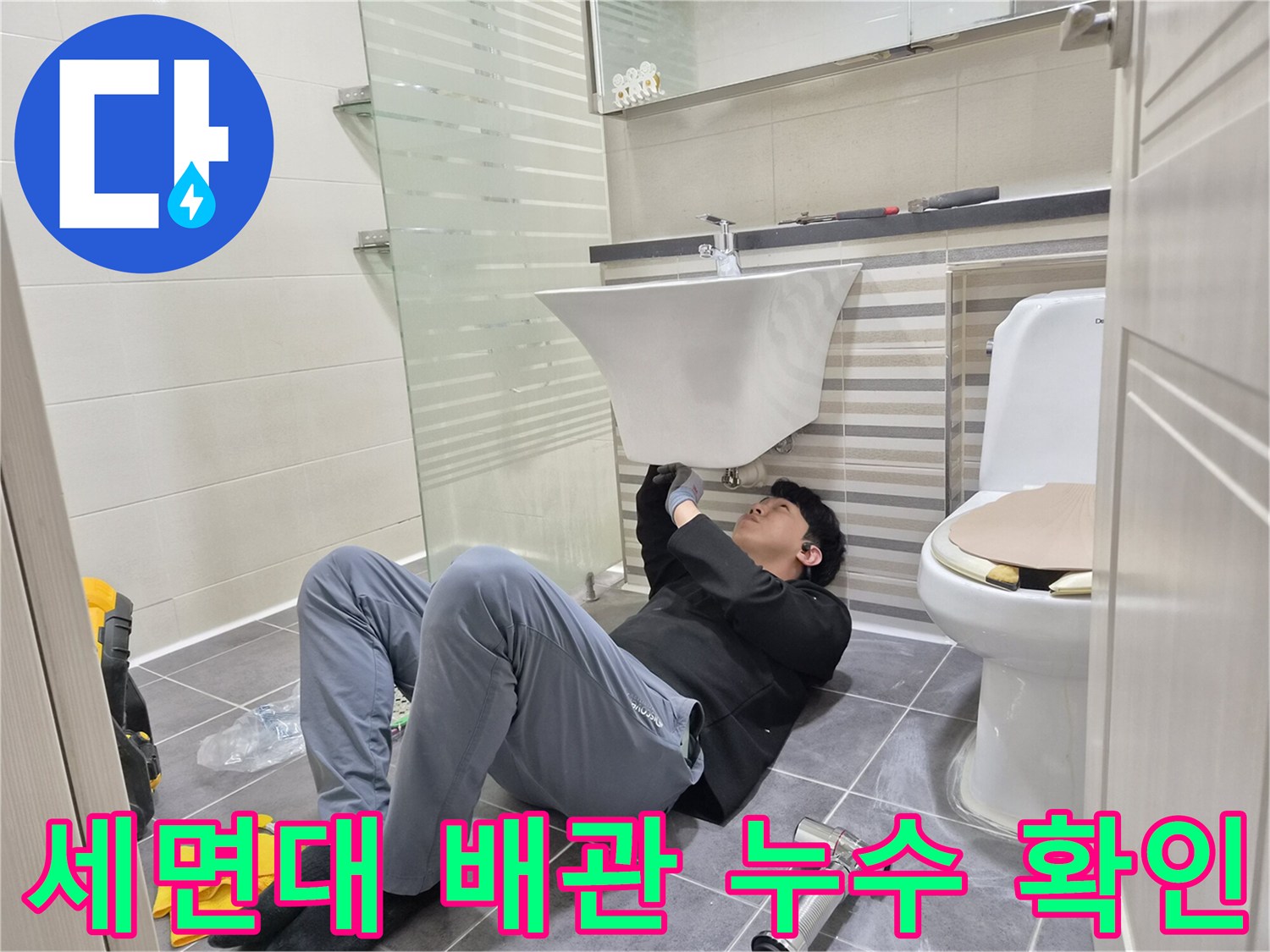 세면대 아래쪽 좁은 공간에서 배관 연결 부위를 검사하는 모습
