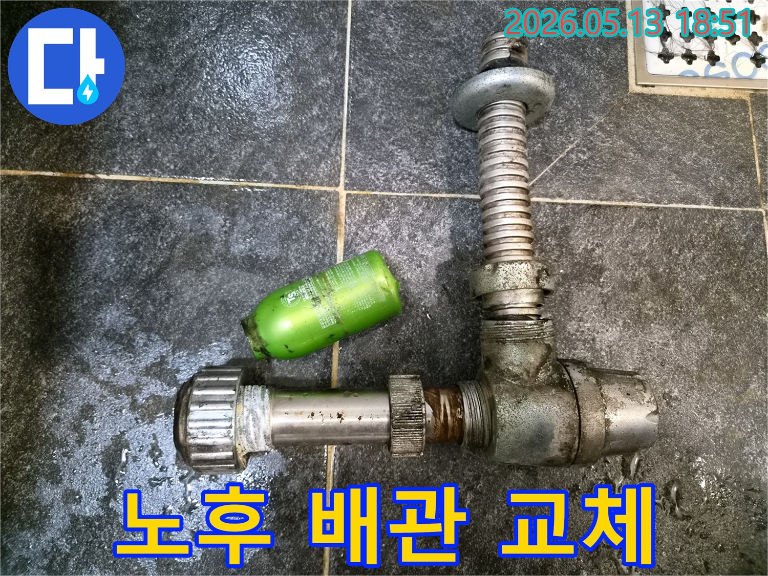 어두운 타일 바닥 위에-녹슬고 오래된 배관 부품과-초록색 샴푸통이 놓여있는-배관 교체 공사 현장