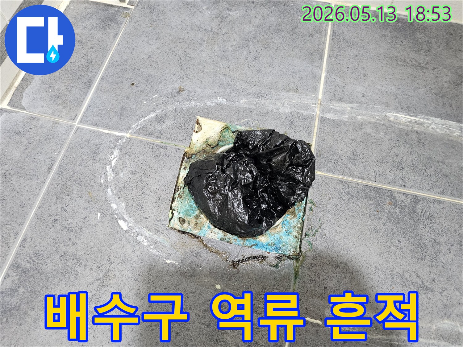 이 사진은-화장실 바닥 배수구의-오랜 부식과-검은 봉투로-막아놓은-상황을-보여주며-주변에-하얀 물자국이-선명합니다