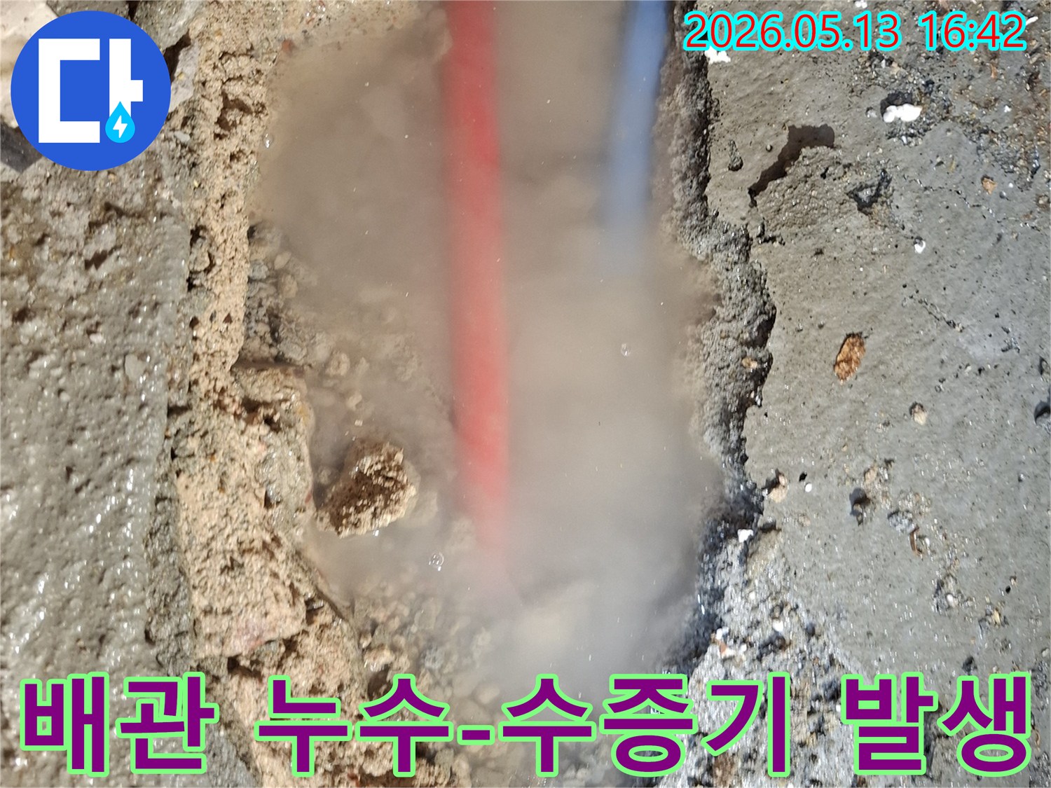 파손된 콘크리트 바닥 아래-붉은색과 푸른색 배관이 노출되고-흙탕물 속에서-수증기가 솟아오르는-누수 현장 이미지
