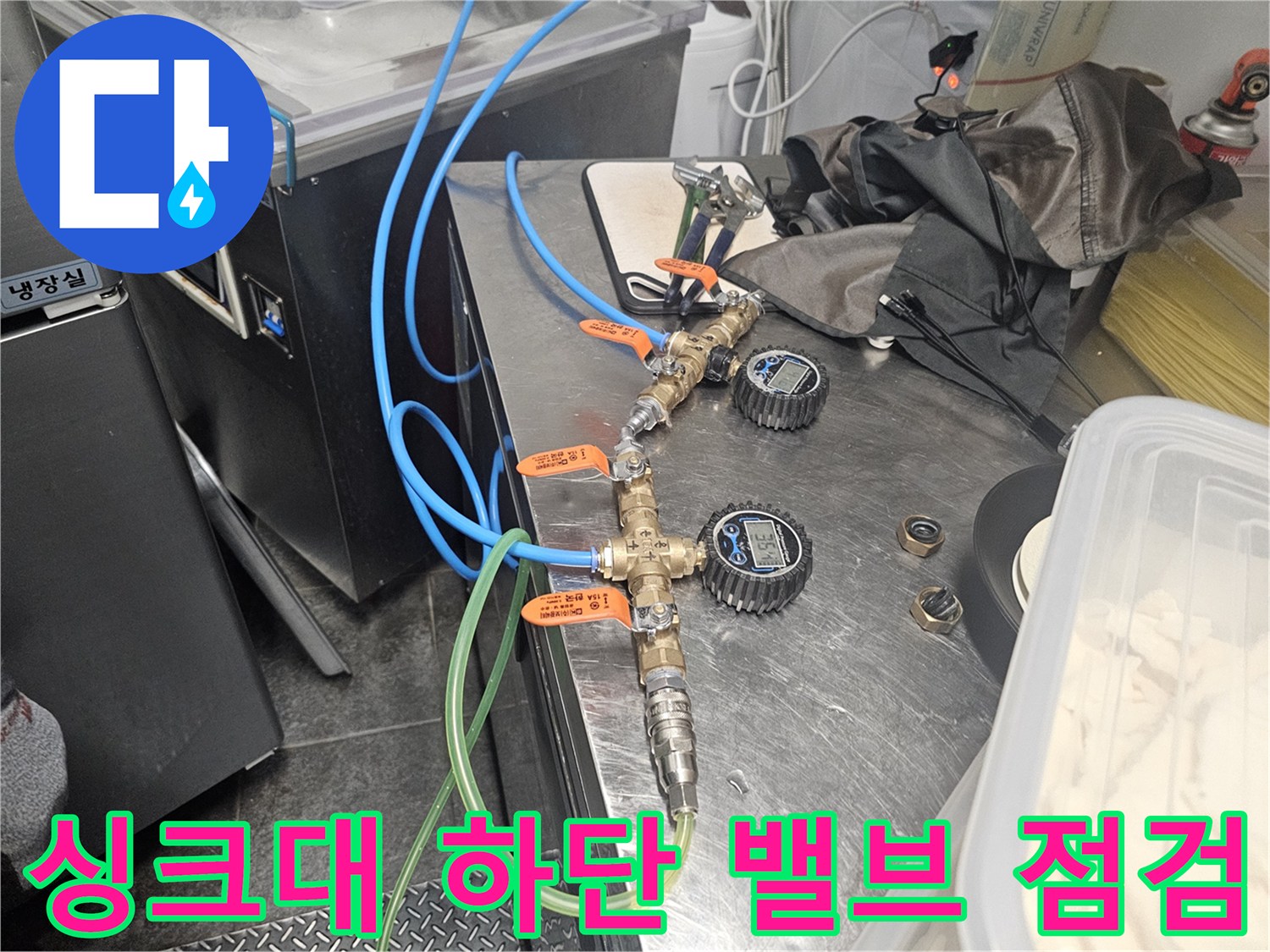 싱크대 아래쪽의 금속 밸브와 파란색 및 초록색 연결 호스