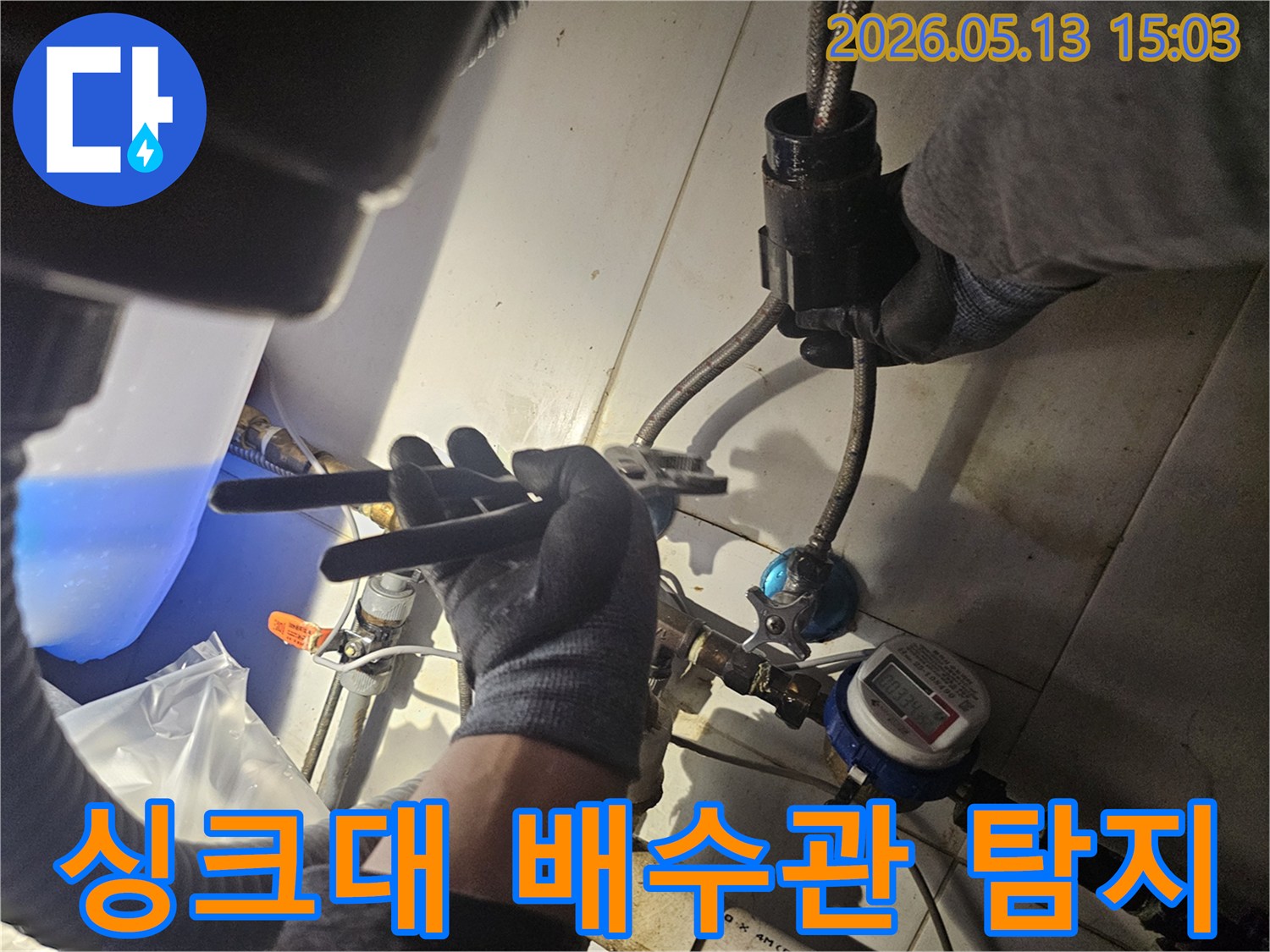 장갑 낀 손이-공구를 이용해-싱크대 아래 배수관의-누수 지점을-탐지하는 모습